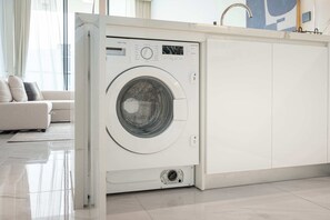 Eine moderne, kompakte Waschmaschine in einer hellen, minimalistischen Küche mit einem sauberen, gefliesten Boden.