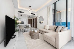 Ein modernes Wohnzimmer mit Flachbildfernseher, einem beigen Sofa, einem runden Couchtisch und einem Essbereich mit Küche im Hintergrund.