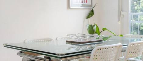A modern dining area with a glass table, white chairs, a large mirror, and a framed picture on the wall.