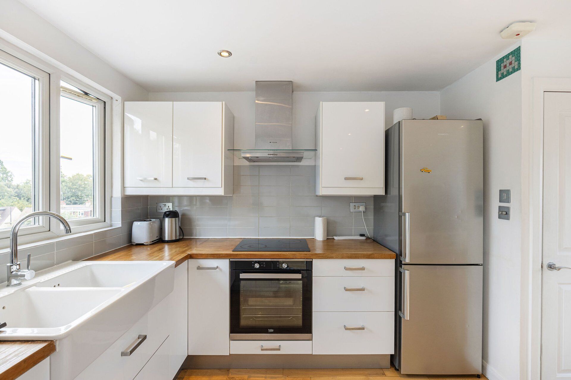 A modern kitchen with white cabinetry, a stainless steel refrigerator, a built-in oven, and a window providing natural light.