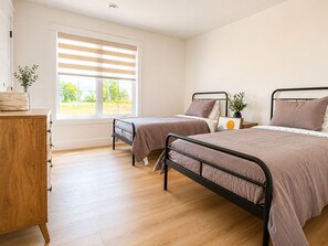 Une chambre avec deux lits, une commode en bois et une fenêtre avec des stores.