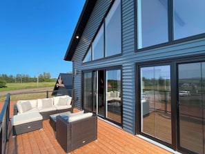 A modern house with a deck, large windows, and outdoor furniture.