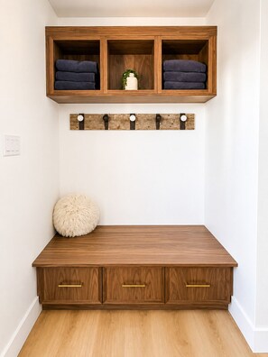 A wooden bench with storage drawers and a shelf above holding folded towels.