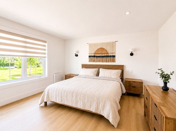 Un dormitorio moderno con una cama grande, cabecera de madera, mesitas de noche, una lámpara de pared y vistas al exterior.