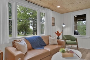A living room with a beige sofa, a green armchair, and a round coffee table with a plant.