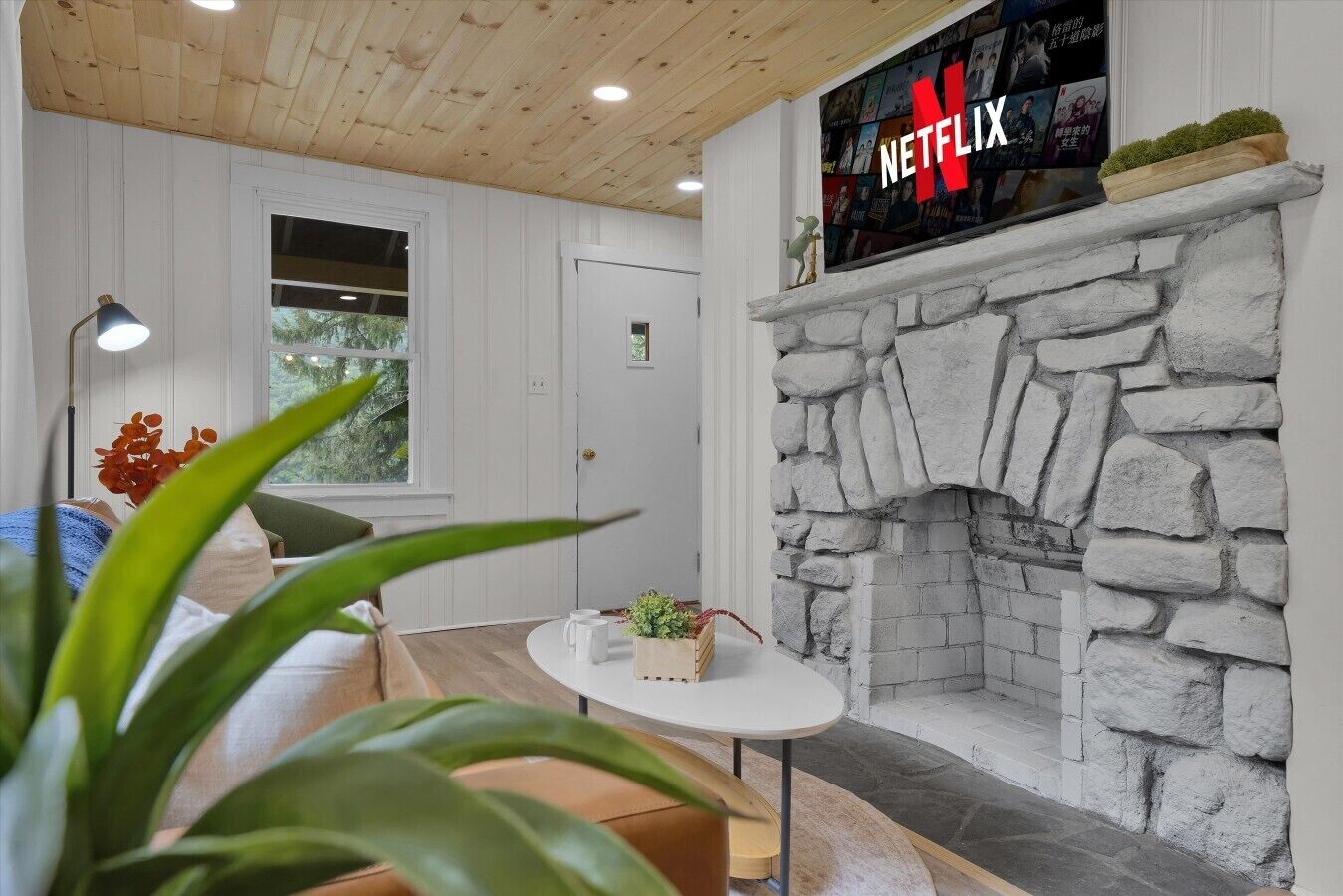 A cozy room with a stone fireplace, a round table, and a large TV screen displaying the Netflix logo.