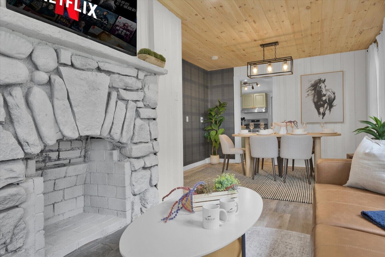 A modern living room with a stone fireplace, a dining area, and a kitchen in the background.