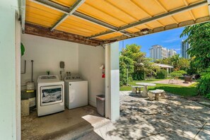 A laundry area with washing machines and a drying rack, a covered outdoor seating area with a table and chairs, and a view of a residential neighborhood with buildings and greenery. - 2BR 2BA Updated Beach Apt with Screened Patio (West Palm Beach)