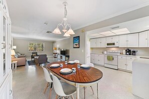 A modern kitchen with white cabinets, a dining area with a wooden table set for four, and a living room with a sofa and TV. - 2BR 2BA Updated Beach Apt with Screened Patio (West Palm Beach)