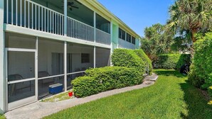 A two-story building with a covered balcony, a lawn, and a palm tree. - 2BR 2BA Updated Beach Apt with Screened Patio (West Palm Beach)