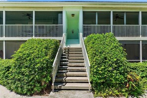 Um edifício com uma escadaria que leva a uma porta verde, cercado por arbustos bem cuidados.