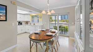 A dining area with a round table, chairs, and a view of the city through large windows. - 2BR 2BA Updated Beach Apt with Screened Patio (West Palm Beach)