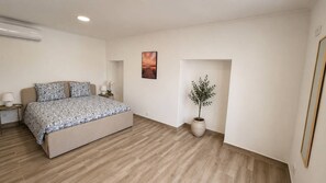 Ein Schlafzimmer mit einem Bett, Nachttischen, einer Topfpflanze und einem Bild an der Wand.