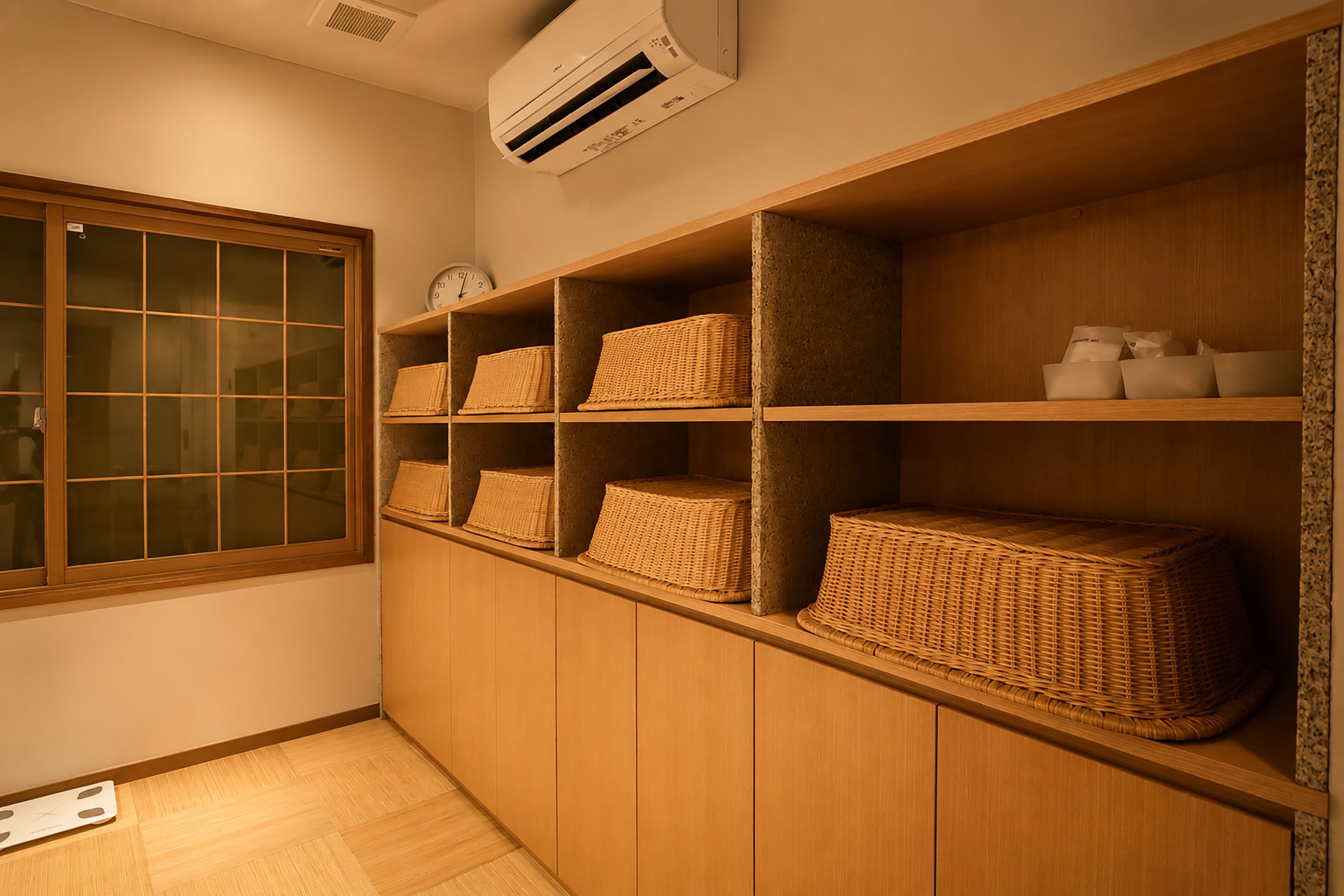 Quarto com estantes de madeira, cestos de vime, um relógio e um ar condicionado.