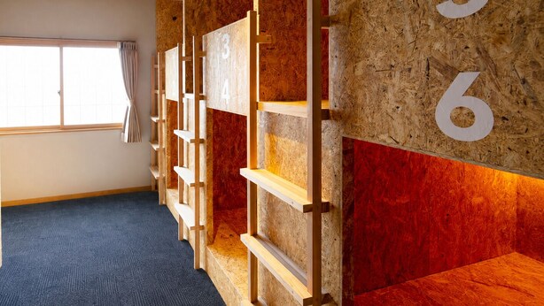 A hotel room with a blue carpet, a window with curtains, and a wall with numbered wooden panels.