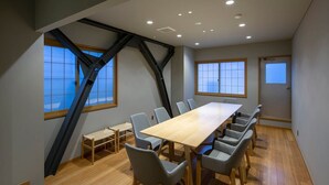 A conference room with a long table and chairs, large windows, and a sloped ceiling.