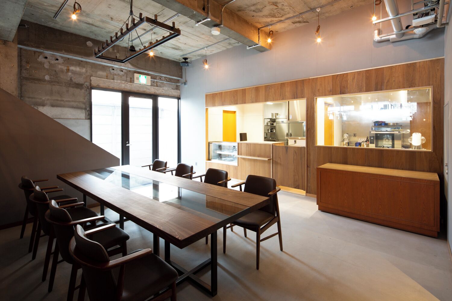 Una sala de reuniones moderna con una larga mesa, sillas y una zona de cocina al fondo.