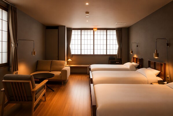 A hotel room with a sofa, two beds, a small table, and a window with curtains.