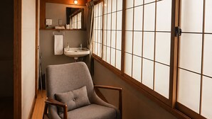A traditional Japanese interior with tatami flooring, a low wooden table, and a seating area with a cushioned chair.
