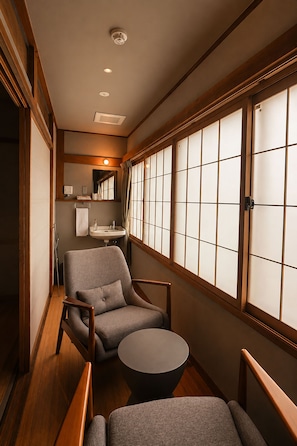 Un intérieur japonais traditionnel avec un sol recouvert de tatamis, une basse table en bois et un coin salon agrémenté d’un fauteuil rembourré.
