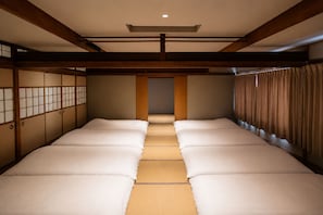 Une pièce de style japonais traditionnel, avec un sol recouvert de tatamis, des portes coulissantes et un couloir central menant à une porte.
