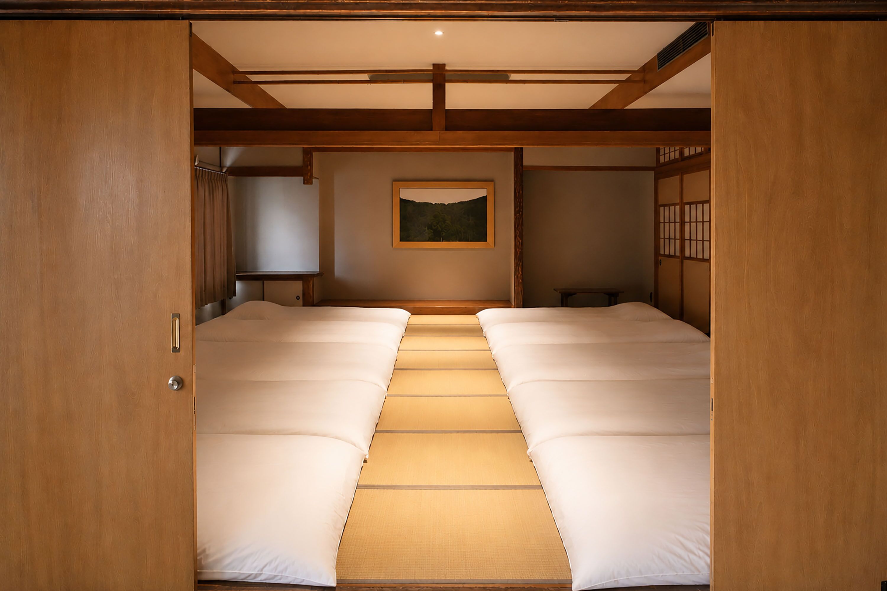 Una habitación tradicional japonesa con suelo de tatami, futón, pantalla shoji y un cuadro en la pared.