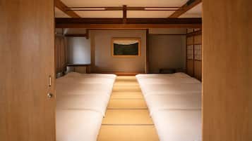 Una habitación tradicional japonesa con suelo de tatami, futón, pantalla shoji y un cuadro en la pared.