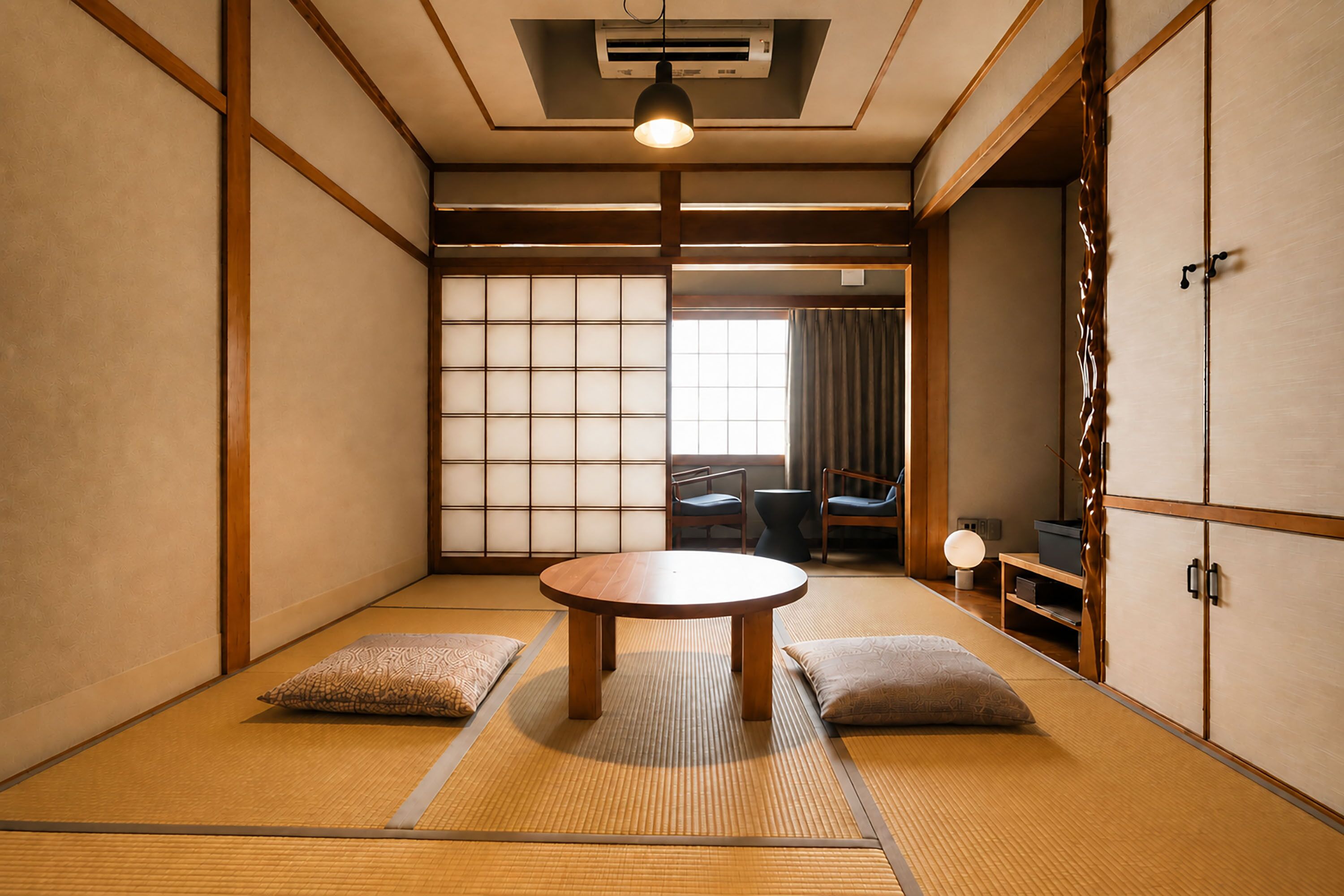 Una habitación japonesa tradicional con suelo de tatami, una mesa baja, cojines, puertas correderas y vistas al exterior.