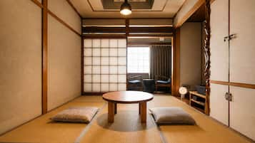 Una habitación japonesa tradicional con suelo de tatami, una mesa baja, cojines, puertas correderas y vistas al exterior.