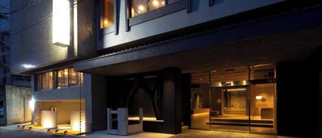 A modern hotel entrance with a covered walkway, a reception desk, and a staircase leading to the entrance.