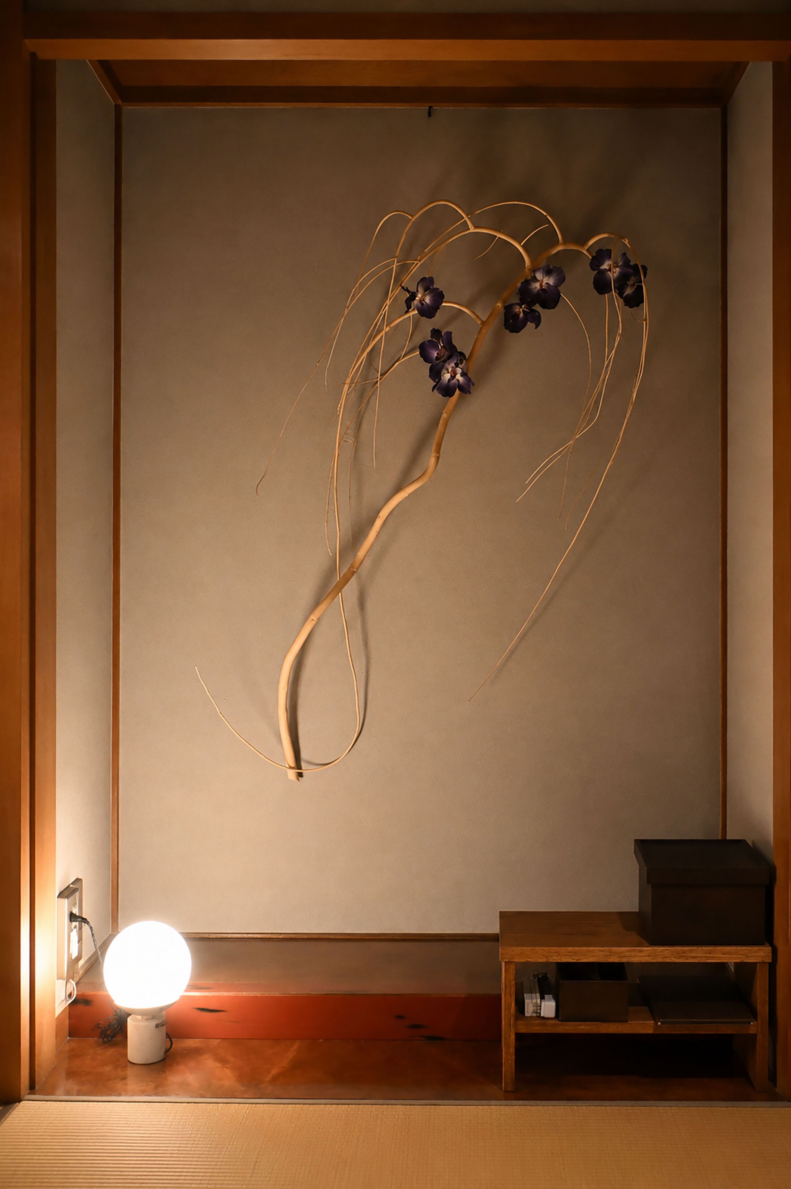Una habitación con piso de madera, una lámpara fijada a la pared y un pequeño estante de madera.