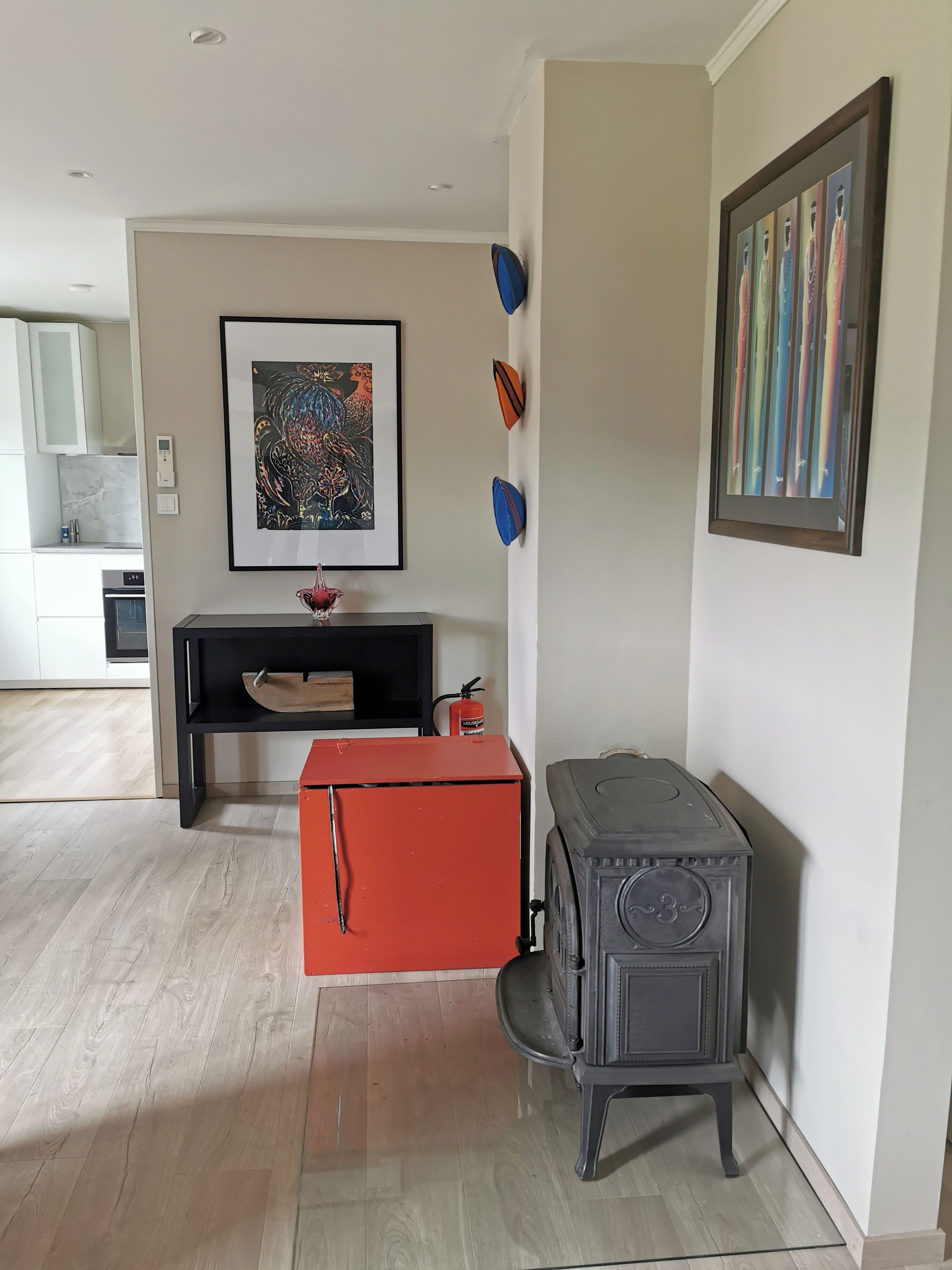 Un salón moderno con chimenea, un caja roja de almacenamiento y una obra de arte enmarcada en la pared.