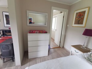 Een slaapkamer met een bed, een dressoir, een spiegel, een lamp en een deur naar een andere kamer.
