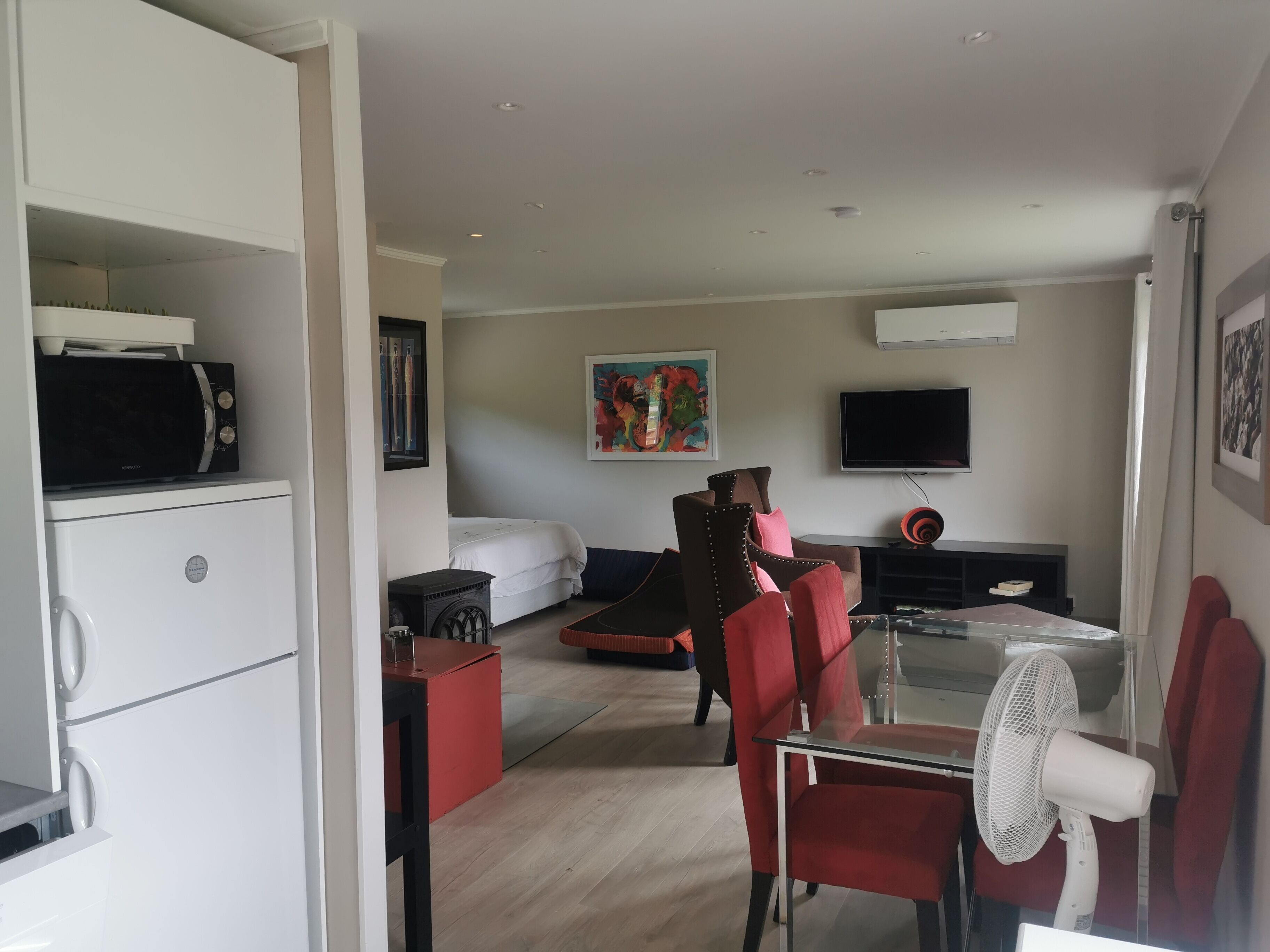 Een moderne woonkamer met een flatscreen televisie, een eethoek met een glazen tafel, en een keuken met een magnetron.
