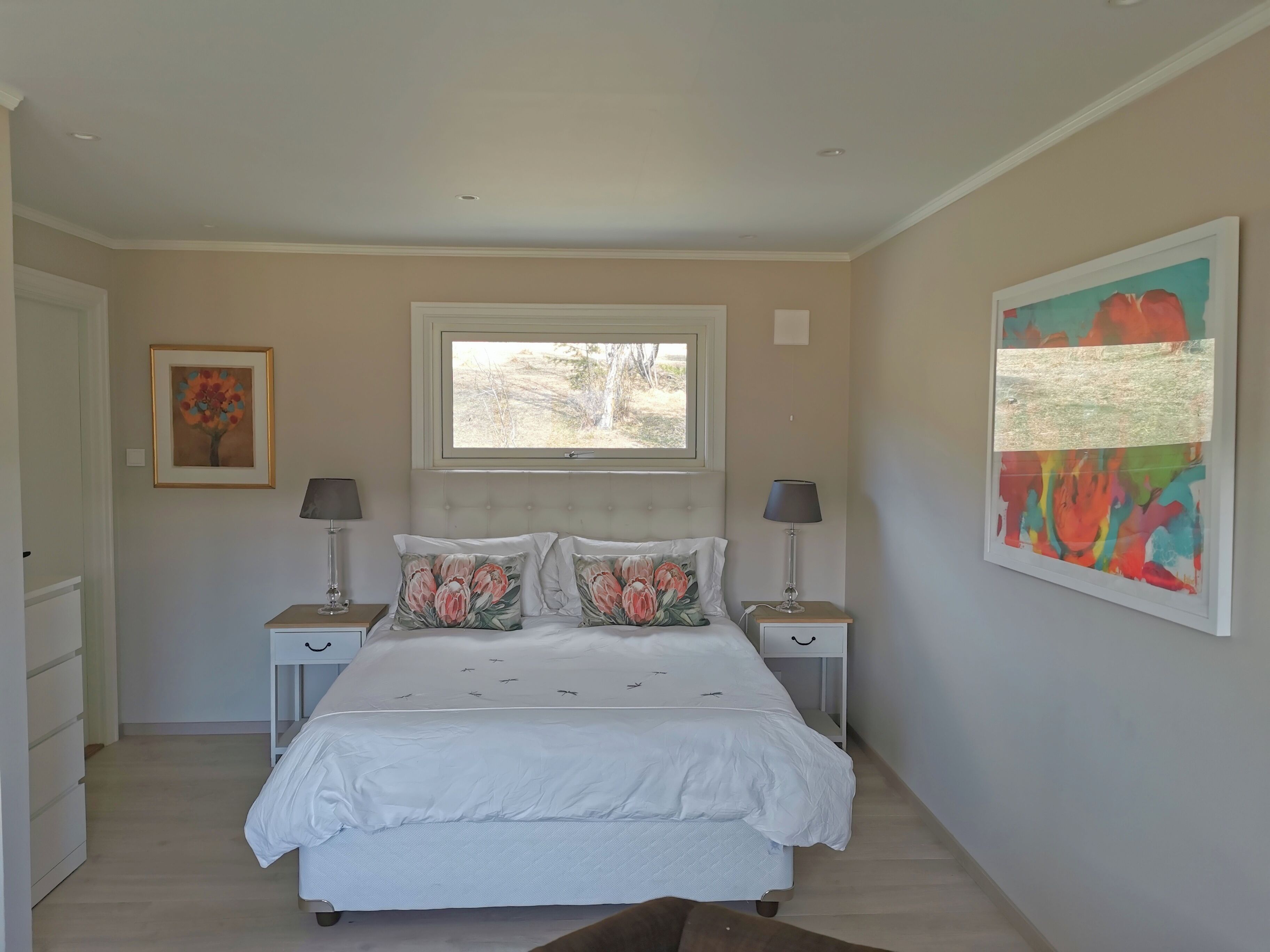 A bedroom with a bed, two bedside tables, a window, and artwork on the walls.