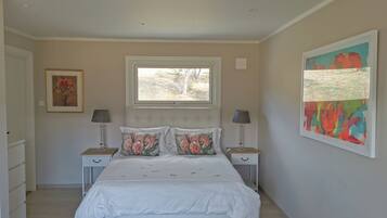 A bedroom with a bed, two bedside tables, a window, and artwork on the walls.