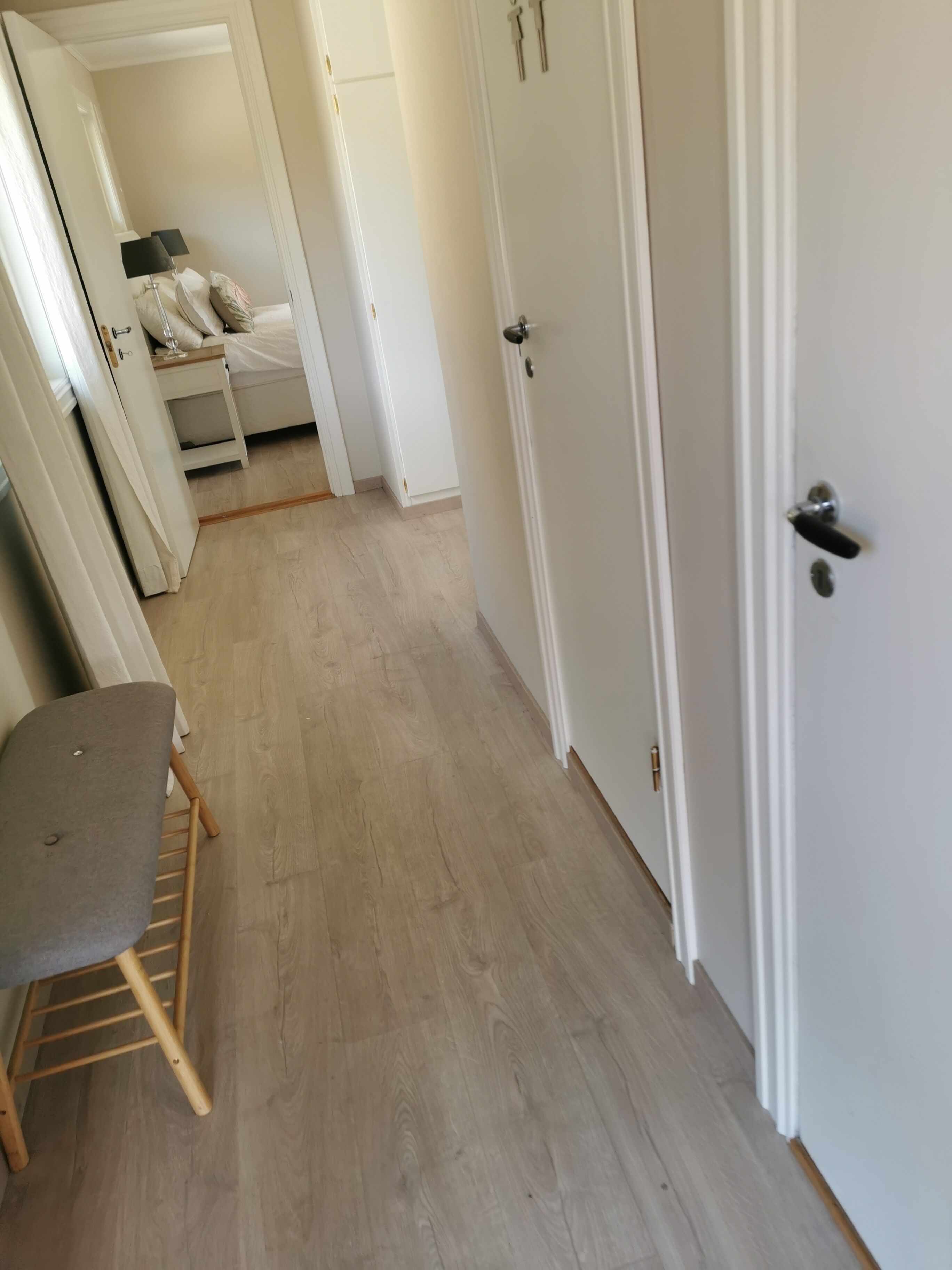 A hallway with a wooden floor, a grey chair, and a bed with white bedding.