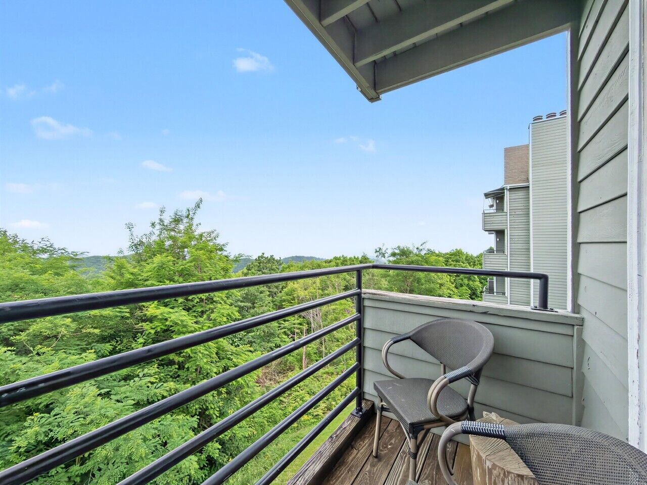 Un balcon doté d’une rambarde en métal, d’une chaise et offrant une vue sur une zone boisée.