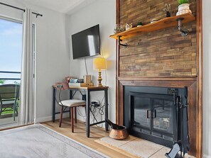 Ein Zimmer mit Kamin, einem an der Wand befestigten Fernseher, einem Tisch mit Lampe und einem Sessel.