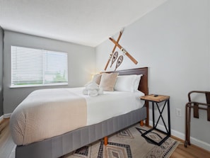 Ein Schlafzimmer mit Bett, Nachttisch und einem Fenster mit Jalousien.