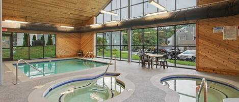 An indoor swimming pool area with two pools, wooden walls, and a view of the outside.