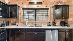 Una cucina con mobili scuri in legno, una lavastoviglie in acciaio inossidabile, una finestra con persiane e un cartello sopra la finestra.