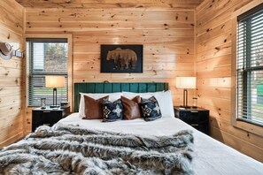 Ein Zimmer mit Holzwänden, einem Bett, Kissen, einem Kopfteil und einem Fenster mit Jalousien.