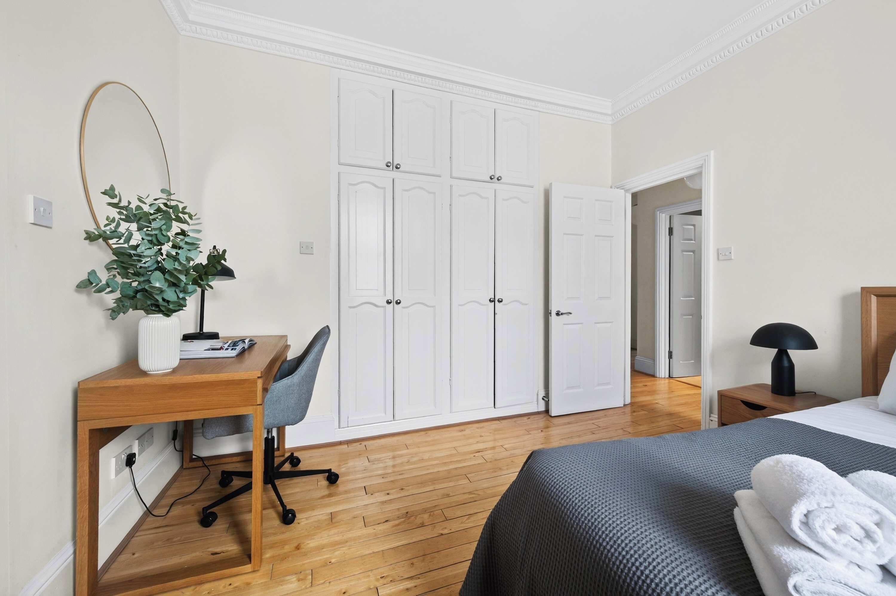 Een slaapkamer met een bed, bureau met stoel, een kledingkast en een plant.