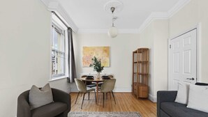 Ein modernes Wohnzimmer mit einer Couch, einem Esstisch mit Stühlen, einem Bücherregal und einem großen Fenster.