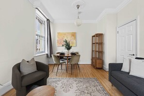 Ein modernes Wohnzimmer mit einer Couch, einem Esstisch mit Stühlen, einem Bücherregal und einem großen Fenster.