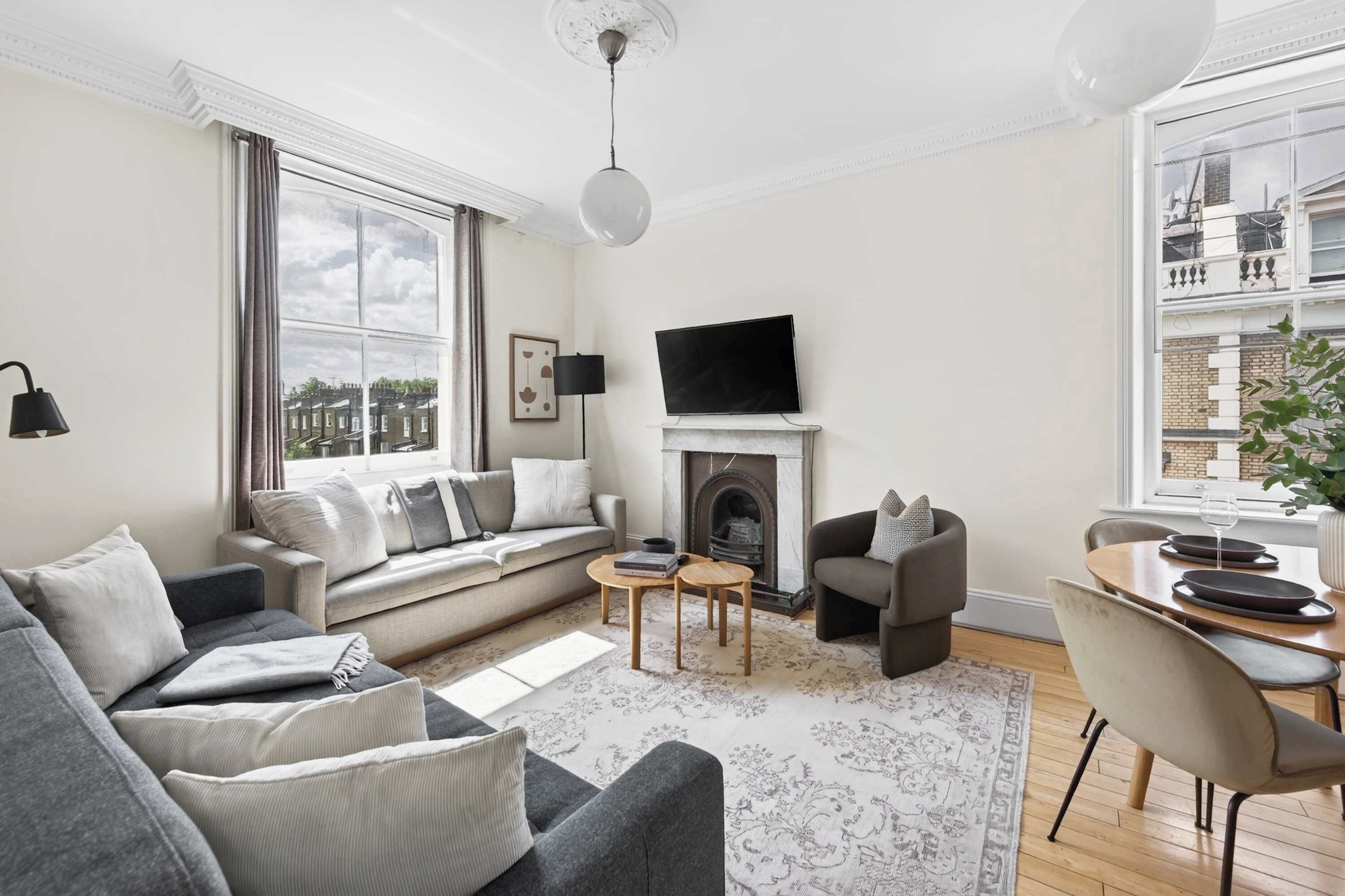 A modern living room with a sofa, armchairs, a fireplace, a television, and a dining area with a table and chairs.