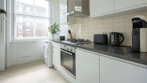 Eine moderne Küche mit weißen Schränken, einem Gasherd, einer Bosch-Kaffeemaschine und Blick auf eine Wohngegend durch das Fenster.