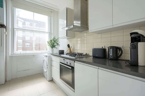 Eine moderne Küche mit weißen Schränken, einem Gasherd, einer Bosch-Kaffeemaschine und Blick auf eine Wohngegend durch das Fenster.