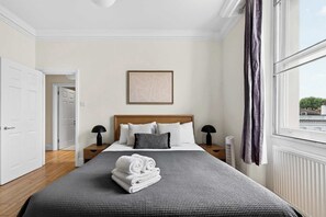 Habitación de hotel con una cama grande, una mesita de noche, un cuadro enmarcado en la pared y una ventana con cortinas.